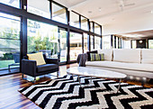 Carpet with black and white zig-zag pattern, coffee table, couch and armchair in front of glass front in open living room
