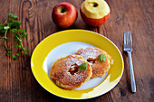 Two battered apple rings with sugar, cinnamon and mint on a yellow plate