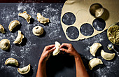 Person shaping empanadas from raw dough