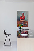 Schwarzer Barhocker vor Kücheninsel unter einem Frauenportrait