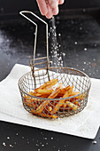 Chips in a frying basket being sprinkled with salt
