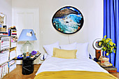 Picture with fluffy frame above bed, potted lemon tree, bedside lamp made from demijohn and open bookshelves in bedroom