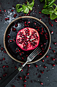 Half a pomegranate and pomegranate seeds on a black surface