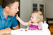A little girl in a high chair feeding her father