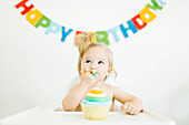 A little girl sitting in a high chair and eating a muffin for her first birthday