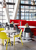 Round tables with yellow and white chairs in restaurant with glass façade