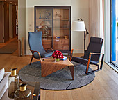 Two armchairs and engineered wooden table on round rug in front of display case