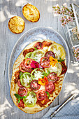 A pizza with colourful tomatoes on a summery outdoor table