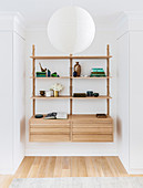 Shelf system with decorative objects, flower vase and books in a wall niche, in front of it a white ball lamp
