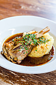 Plated lamb shank in a rich gravy on potato mash garnished with chives on a wooden background
