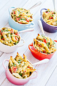 Mini servings of pasta bake with peas, cherry tomatoes in a creamy white sauce served in small colourful pots with forks