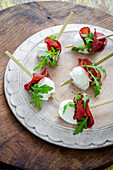 Buffalo mozzarella bites with bresaola and fresh rocket leaves canapes on a white wooden board and wooden background