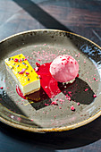 Passion fruit cheesecake slice served with strawberry sorbet on a dark plate and background
