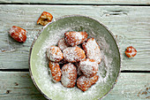 A plate of homemade, deep-fried pastries with icing sugar (seen from above)