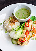 Thai chicken thighs with fresh chilly, cucumber and tomato salad, white basmati rice and spring onion broth on a white plate