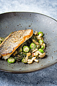 Pan fried trout fillet on a spinach, okra and wild mushroom sauteed in a dark bowl on a marble table