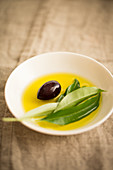 Olive oil with a black olive and an olive sprig in a bowl