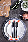 A place setting with a grey plate, white plates and black cutlery