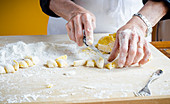 Italian chef cutting fresh homemade potato gnocchi into cubes with white flour on wooden board