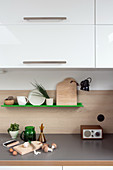 Chopping board on grey worksurface below green shelf and wall units in kitchen