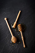 Three honey dippers with honey on a black slate