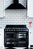 Black gas cooker and extractor hood on white subway wall tiles in kitchen