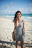 A young woman on a beach wearing a grey, wraparound dress