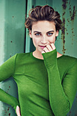 A short-haired woman standing in front of green background wearing a green jumper