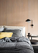 Double bed and wall lamp on room divider with wooden paneling