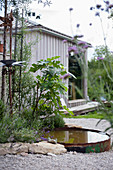 Teich mit rostiger Metallbegrenzung im Garten vor einem Holzhäuschen