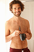 A young, topless man holding a cup of coffee