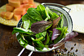 Salad ingredients: mixed leaves being washed in a sieve