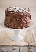 A three-layer chocolate cream cake on a cake stand