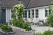 Hof mit Blumenbeeten und Terrasse vorm weißen Schwedenhaus