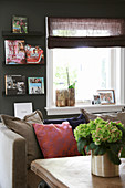 View of sofa with scatter cushions, window and bookcase on dark wall across coffee table