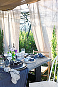 Table set for summer party below wooden frame covered with fabric awnings
