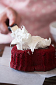 A cook decorating a red velvet cake with icing