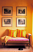 Four pictures on yellow wall above antique couch with striped scatter cushions