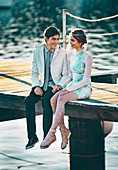 An elegantly dressed young couple sitting on a jetty