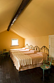 Four wrought iron single beds in attic room with black-tiled floor