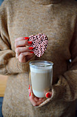 Frau hält ein Glas Caffe Latte mit herzförmigem Cookie