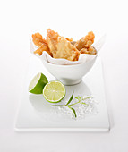 Battered fish in a bowl with lime halved, sea salt and sprig of fresh lime leaves