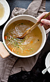 A woman's hands stirring a pot of chicken noodle soup with a wooden spoon