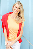 Junge blonde Frau in gelbem T-Shirt mit rotem Pulli um Schultern