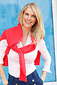 A young blonde woman wearing a white shirt with a red jumper over her shoulders