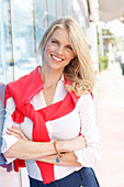 Junge blonde Frau in weißem Hemd mit rotem Pulli um Schultern