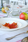 Red autumn leaf on white plate and apples on set table