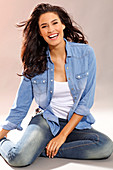 A young brunette woman wearing a white top, a denim shirt and jeans