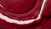 Cream being poured into beetroot soup
