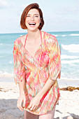 A red-haired woman by the sea wearing a beach dress